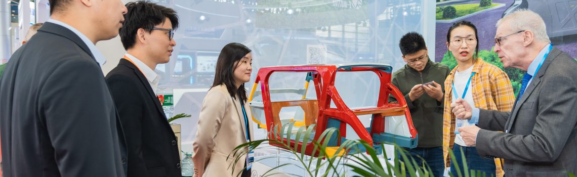 People standing around and talking near the Steel E-Motive 3d model at a trade show